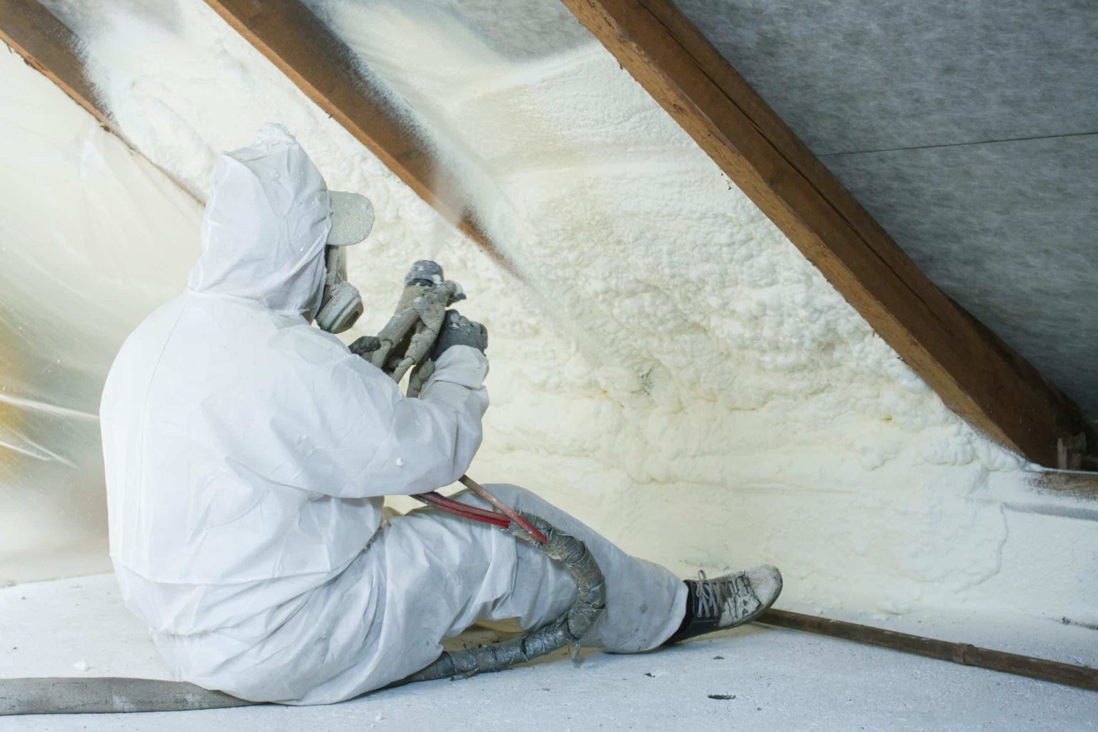 Worker spraying insulation in attic space.