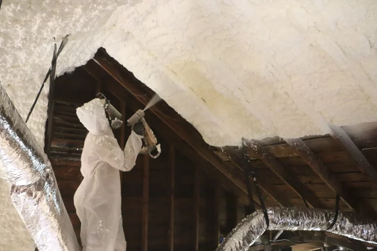 Worker spraying insulation on wooden wall.